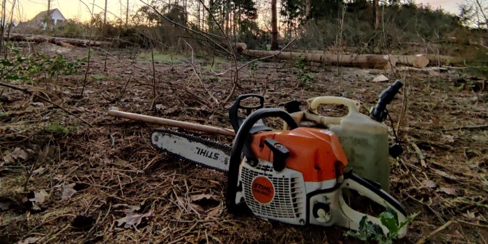 Stihl kettingzaag met jerrycan staat in een bosgebied met op de achtergrond gezaagde boomstammen.